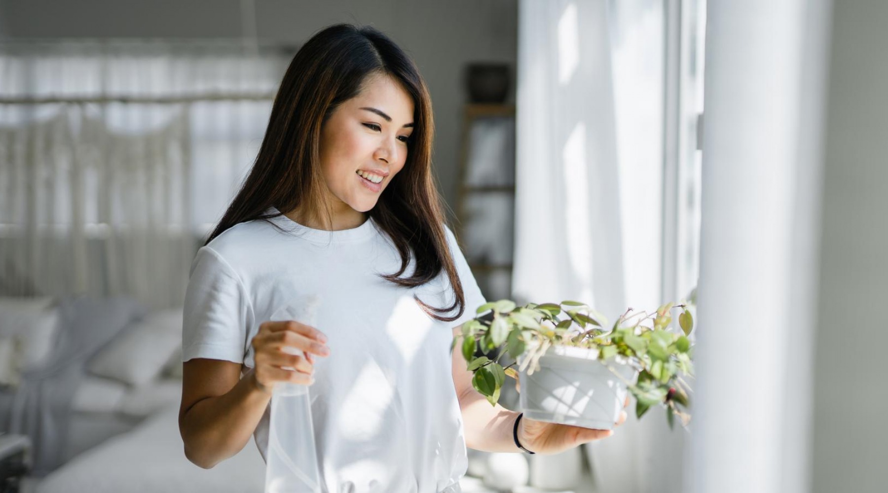 A woman holding a plant in a sunny window in Pinnacle Apartments